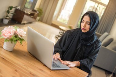 Genç Müslüman kadın evde dizüstü bilgisayar kullanıyor..