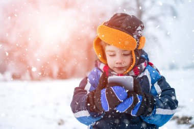 Kışın küçük çocuk soğuk karlı bir günde telefon ya da tablet kullanır.