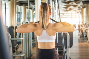 Sportif bir kadının spor salonundaki halat çekme makinesinde barfiks çekişi.