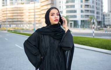 Abaya 'daki çekici Müslüman kadın şehir caddesinde cep telefonuyla konuşuyor.