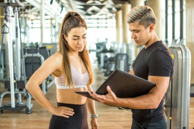 Genç bir kadın, erkek fitness eğitmeniyle çalışma sürecini tartışıyor..