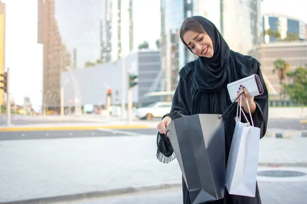 Happy young Arab woman looking into shopping bag on the street