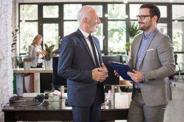 Resmi takım elbiseli genç ve yaşlı işadamları ofiste bir toplantının belgesini tartışıyorlar..