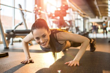 Fitness genç kadın şınav çekiyor ve spor salonunda kameraya bakıyor..