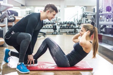 Spor salonunda birlikte egzersiz yapan sporcular. Yakışıklı bir adam spor salonunda otururken güzel bir kıza yardım ediyor..