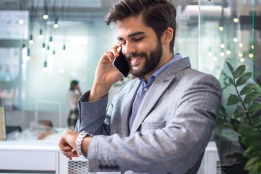 Çekici erkek ofiste cep telefonuyla konuşurken saati kontrol ediyor..