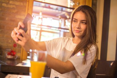 Genç bir kız restoranda cep telefonuyla selfie çekiyor.