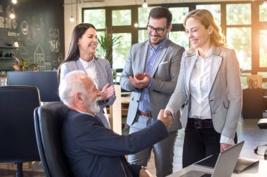 Smiling mature businesswoman handshaking with senior businessman at meeting negotiation. Colleagues clapping hands and celebrating successful agreement clipart