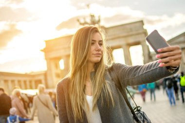 Berlin 'de Brandenburger Tor' un önünde gün batımında selfie çeken güzel bir genç kadın..