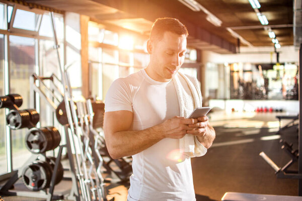 Portrait of handsome guy text messaging on his mobile phone at gym
