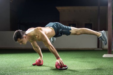 Genç kaslı adam amuda kalkıyor ve jimnastik salonunda kettlebell üzerinde dengede duruyor..