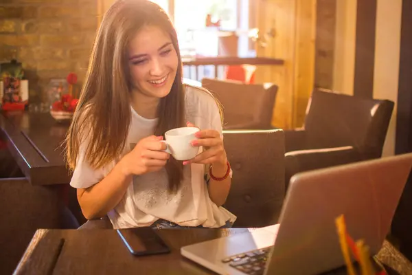 若い十代の少女はコーヒーカップを保持し バーのラップトップで何かを読んで — ストック写真
