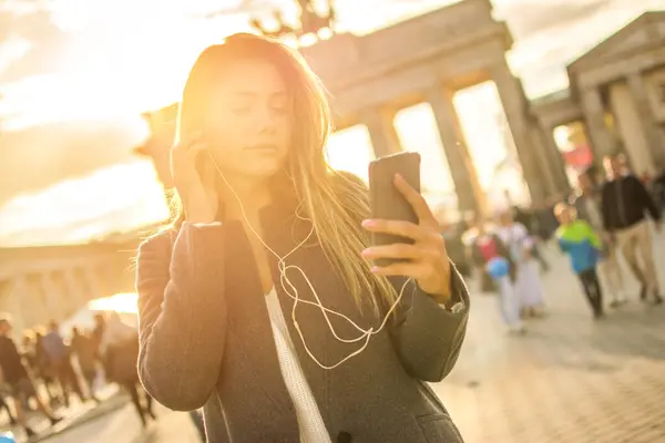 Mujer Joven Escuchando Música Por Teléfono Mientras Camina Cerca Puerta — Foto de Stock