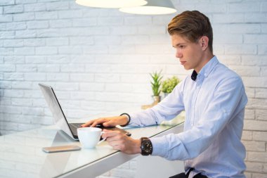 Genç adam kahve içiyor ve evde dizüstü bilgisayar kullanıyor..