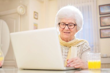 Evde dizüstü bilgisayar kullanan yaşlı bir kadın.