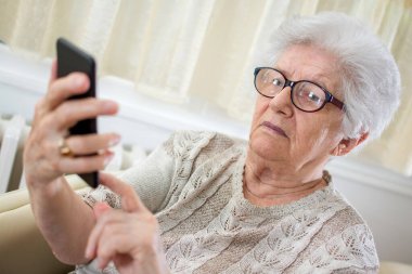 Evde akıllı telefon kullanan kafası karışmış yaşlı bir kadın..