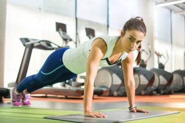 Slim fitness genç kız atkuyruğu ile spor salonunda planking egzersizi yapıyor..