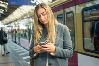Tren istasyonunda tren beklerken cep telefonu kullanan genç bir kadın..