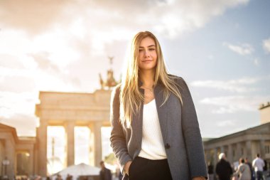 Almanya, Berlin 'de Brandenburger Tor' un önünde gülümseyen modaya uygun genç bir kadının portresi