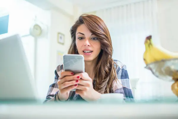 Masada oturan genç bir kadın akıllı telefon kullanıyor.