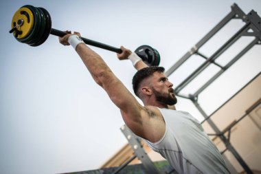 Spor salonunda koltuk değneklerini kaldıran kaslı genç adam..