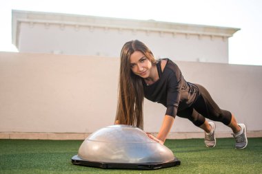 Fit kadın açık havada bosu topunda şınav çekiyor..