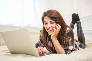 Genç gülümseyen kadın yatakta yatarken ve dizüstü bilgisayar kullanarak.