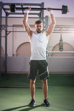 Spor salonunda halterle egzersiz yapan kaslı bir adamın tam boy portresi..