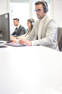 Ofiste bilgisayarla çalışan kulaklıklı bir erkek müşteri destek operatörü. Masadaki alanı kopyala