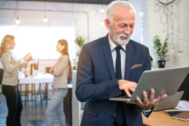 Görevdeyken dizüstü bilgisayar kullanan kıdemli iş adamının portresi.