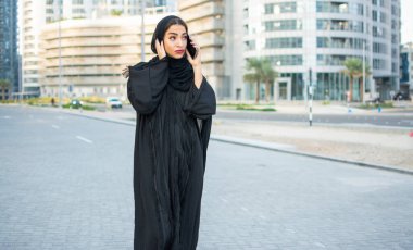 Güzel bir Arap kadını sokakta telefonla konuşuyor.