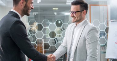 İki gülümseyen iş adamı ofiste el sıkışıyor.