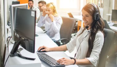 Çağrı merkezindeki müşteriyle konuşan gülümseyen genç bir bayan.
