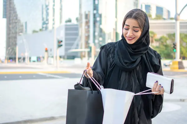 Beautiful young middle eastern Arab woman looking at stuff from the shopping bags on the street