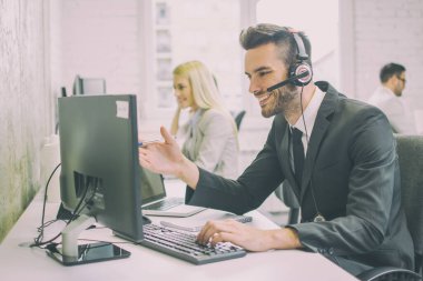 Ofiste bilgisayarla çalışan gülümseyen yakışıklı bir erkek çağrı merkezi operatörü.