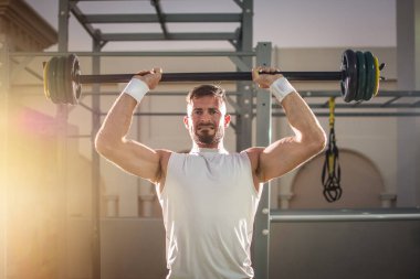 Spor salonunda halteri kaldıran güçlü yakışıklı adam..