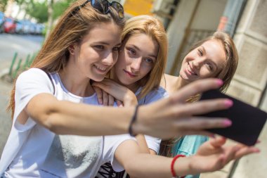 Genç kızlar açık havada akıllı telefonlarda selfie çekiyorlar.