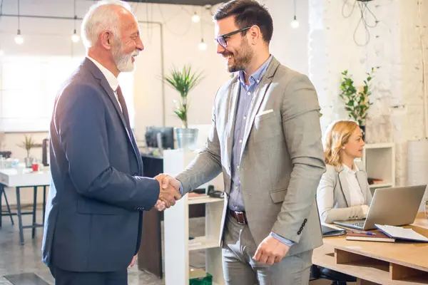 Üst düzey yönetici ofiste genç bir çalışanla tokalaşıyor..
