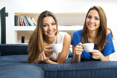 Genç ikiz kardeşler kanepede uzanıp kahve fincanları tutuyorlar.