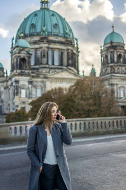 Berlin, Almanya 'da Berliner Dom' un önünde sokakta konuşurken cep telefonuyla konuşan güzel genç bir iş kadını..