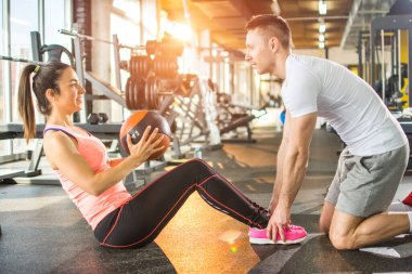 Sportif kız spor salonundaki spor hocasının yardımıyla spor topuyla mekik çekiyor.