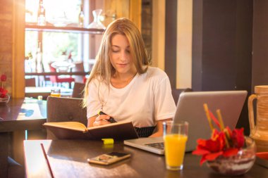Üniversite öğrencisi kız masada otururken ders çalışıyor ve notlar yazıyor.