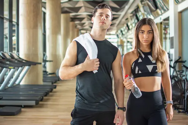 Spor salonunda bir şişe su ve havluyla güzel genç sporcular.