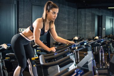 Spor salonunda formda bir kız bisiklet sürüyor..
