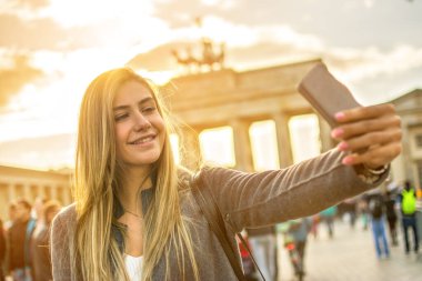 Telefonla gülümseyen kız Berlin 'deki Brandenburg kapısının önünde selfie çekiyor..