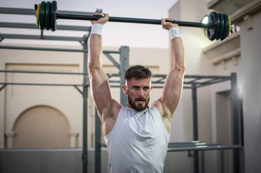 Spor salonunda koltuk değneklerini kaldıran kaslı genç adam..