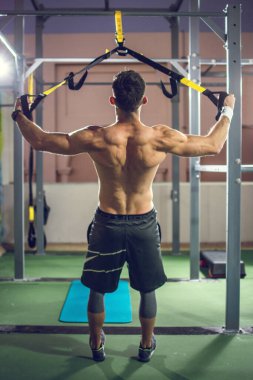 Spor salonunda askıları olan yakışıklı, kaslı bir adamın antrenmanının arkası..