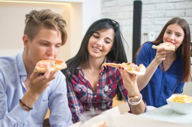 Gülümseyen arkadaşlar evde pizza yiyorlar.