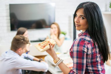 Evde arkadaşlarıyla pizza yiyen genç bir kadın.