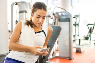 Spor salonunda kulaklığı ve akıllı telefonu olan genç bir kadın..
